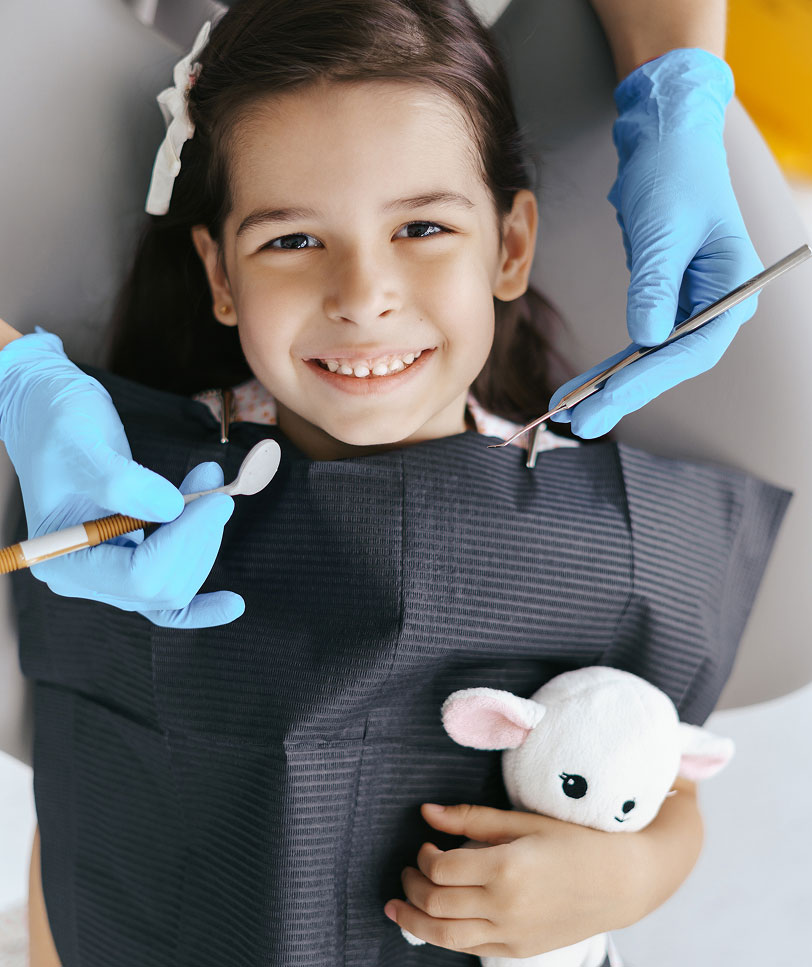 child smiling in dental chair holding stuffed animal
